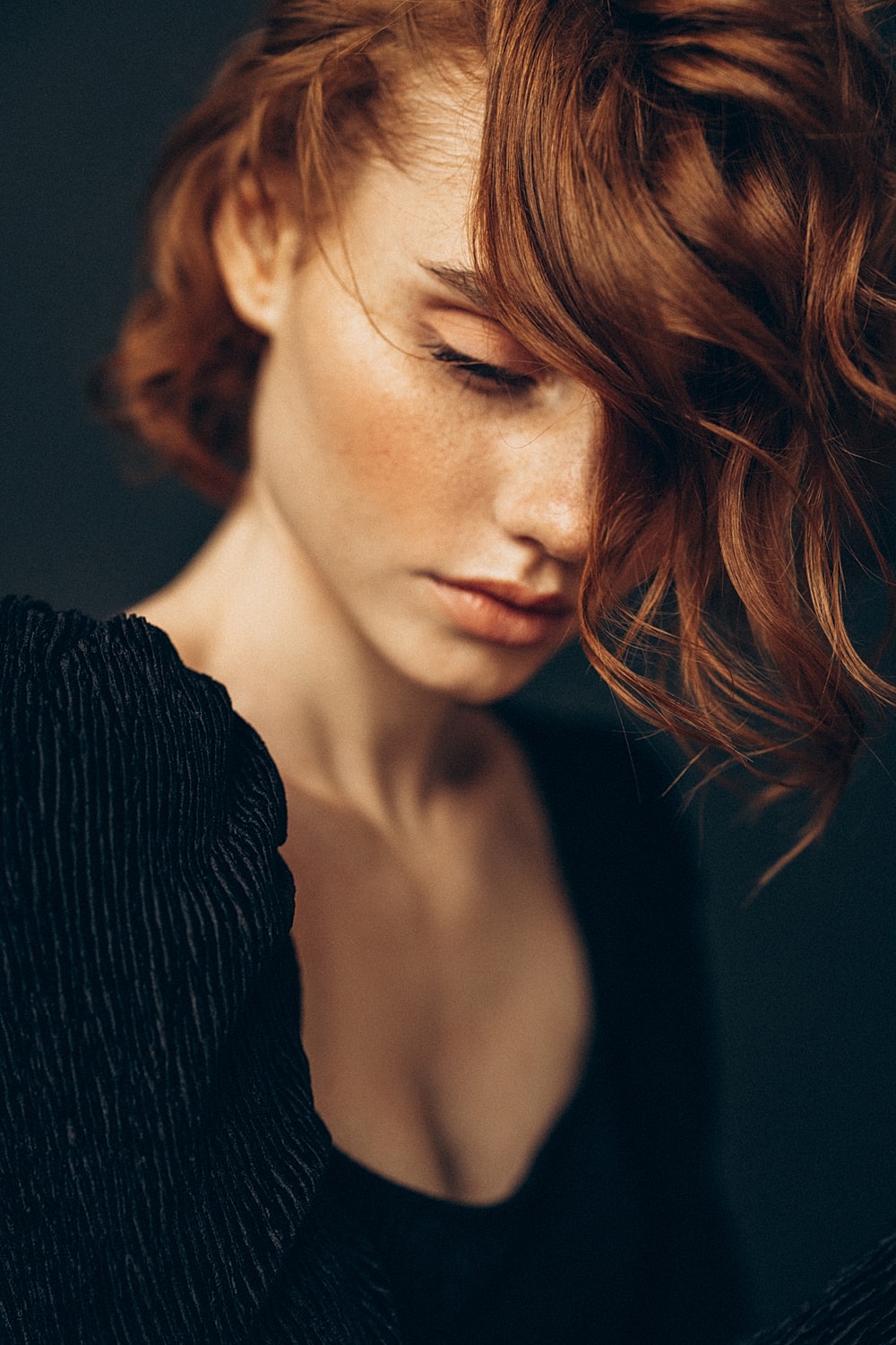 Woman with wavy red hair gazing downwards.
