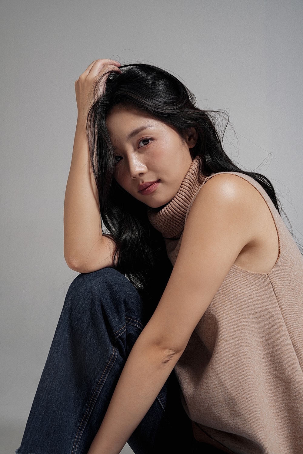 Woman with long black hair, sitting thoughtfully.